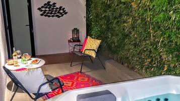 A hot tub area with a table and chairs, a decorative wall, and a small table with drinks.