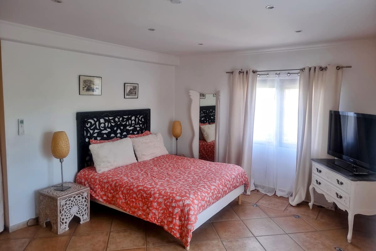 A bedroom with a bed, a TV, a bedside table, a lamp, and a window with curtains.