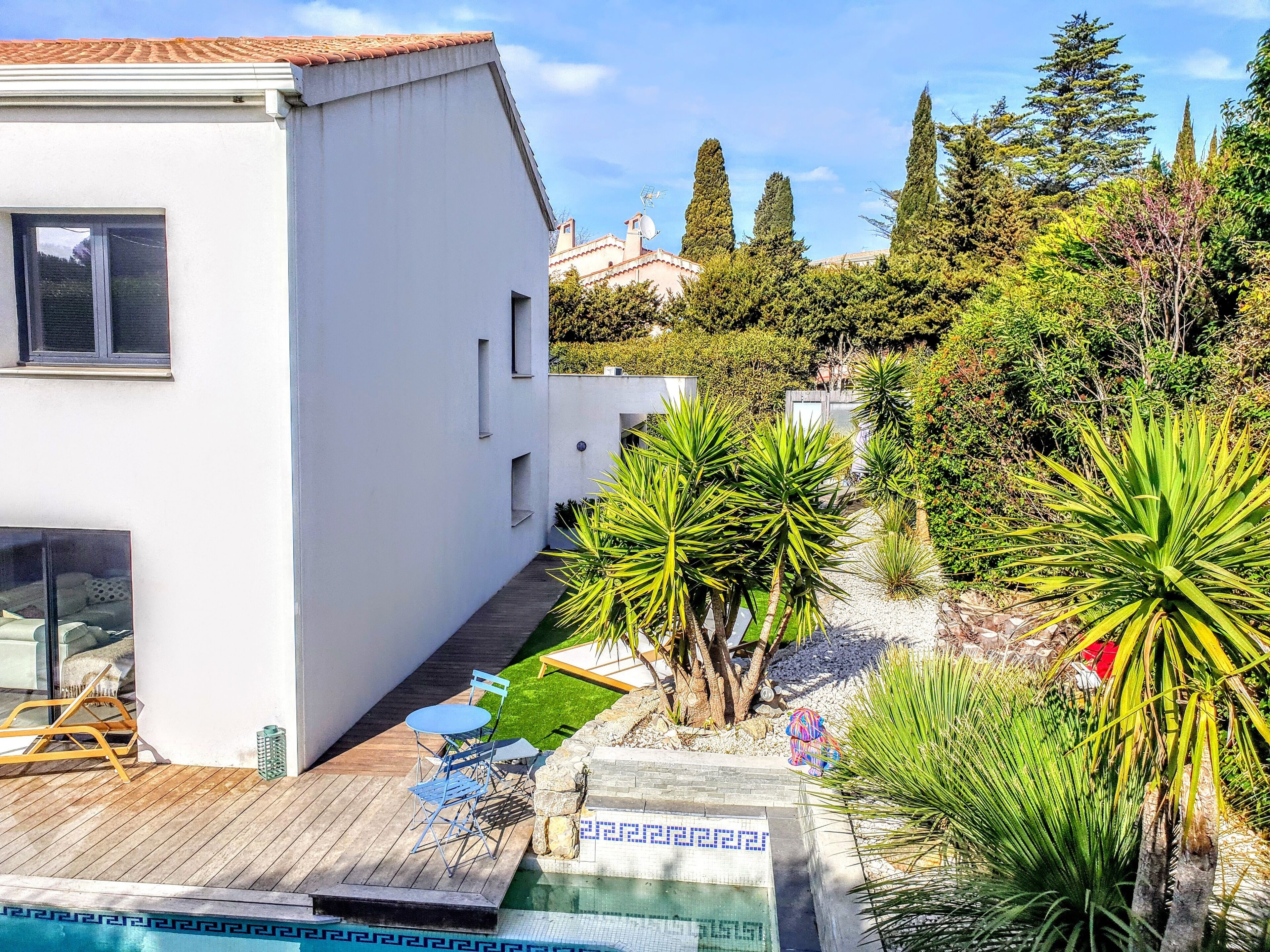 Une maison moderne dotée d’une piscine, entourée de différentes plantes et arbres.