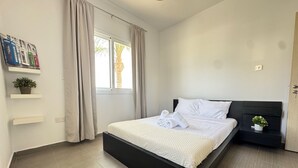 Une chambre à coucher moderne avec un cadre de lit noir, du linge de lit blanc et une petite table de chevet agrémentée d’une plante.
