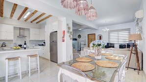 Une cuisine moderne avec des meubles blancs, un réfrigérateur en acier inoxydable et un coin repas doté d’une table en verre et de sets de table en fibres tressées.