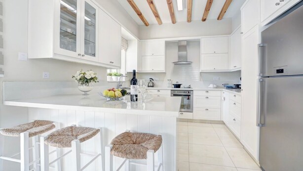 Une cuisine moderne avec des meubles blancs, un îlot central doté de tabourets de bar et un réfrigérateur en acier inoxydable.