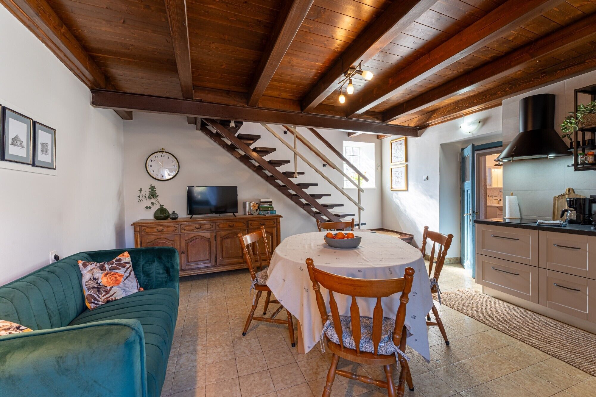 Una sala de estar acogedora con un sofá verde, una mesa de comedor con sillas, un televisor y una escalera que sube a otro nivel.