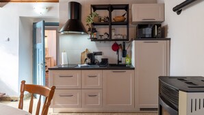 Une cuisine compacte avec des meubles blancs, une hotte noire, un four à micro-ondes et une cuisinière. On peut apercevoir une chaise en bois et une petite table à manger.