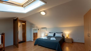 Une chambre avec un puits de lumière, un lit avec des oreillers, des lampes de chevet, une armoire et un plancher en bois.