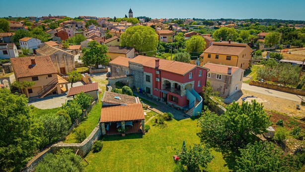 Vue aérienne d’un quartier résidentiel, où l’on aperçoit un imposant bâtiment rouge doté d’un escalier en colimaçon et d’un petit jardin.