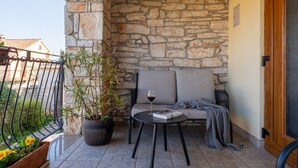 Un espace extérieur aménagé avec des murs en pierre, comprenant une table et des chaises, une plante en pot et une porte située à droite.