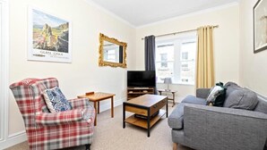 A living room with a plaid armchair, a grey sofa, a television, and a coffee table. - JOIVY Rose Street Hideaway (Edinburgh)