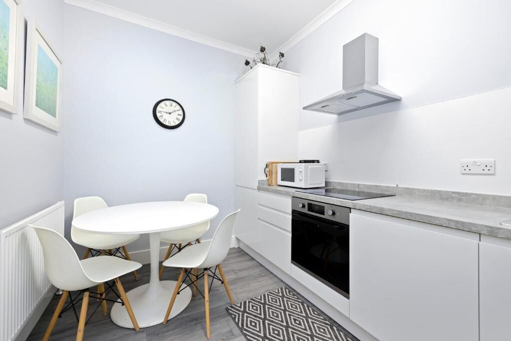 A modern kitchen with white cabinetry, a microwave, an oven, and a clock on the wall.