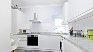A compact kitchen with white cabinetry, a microwave, a toaster, and a washing machine. - JOIVY Rose Street Hideaway (Edinburgh)