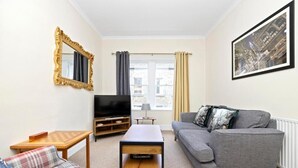 A living room with a grey sofa, a wooden coffee table, a television, and a framed picture on the wall. - JOIVY Rose Street Hideaway (Edinburgh)