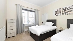 A bedroom with a bed, bedside tables, a desk, and a window with curtains. - JOIVY Rose Street Hideaway (Edinburgh)