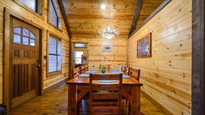 Een houten cabin met daarin een eettafel, stoelen, een kroonluchter en een bordje met de tekst 'Cabin Welcome'.