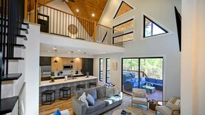 Un vaste espace de vie doté d’un haut plafond, une cuisine avec un îlot central et un balcon aménagé avec des sièges d’extérieur.