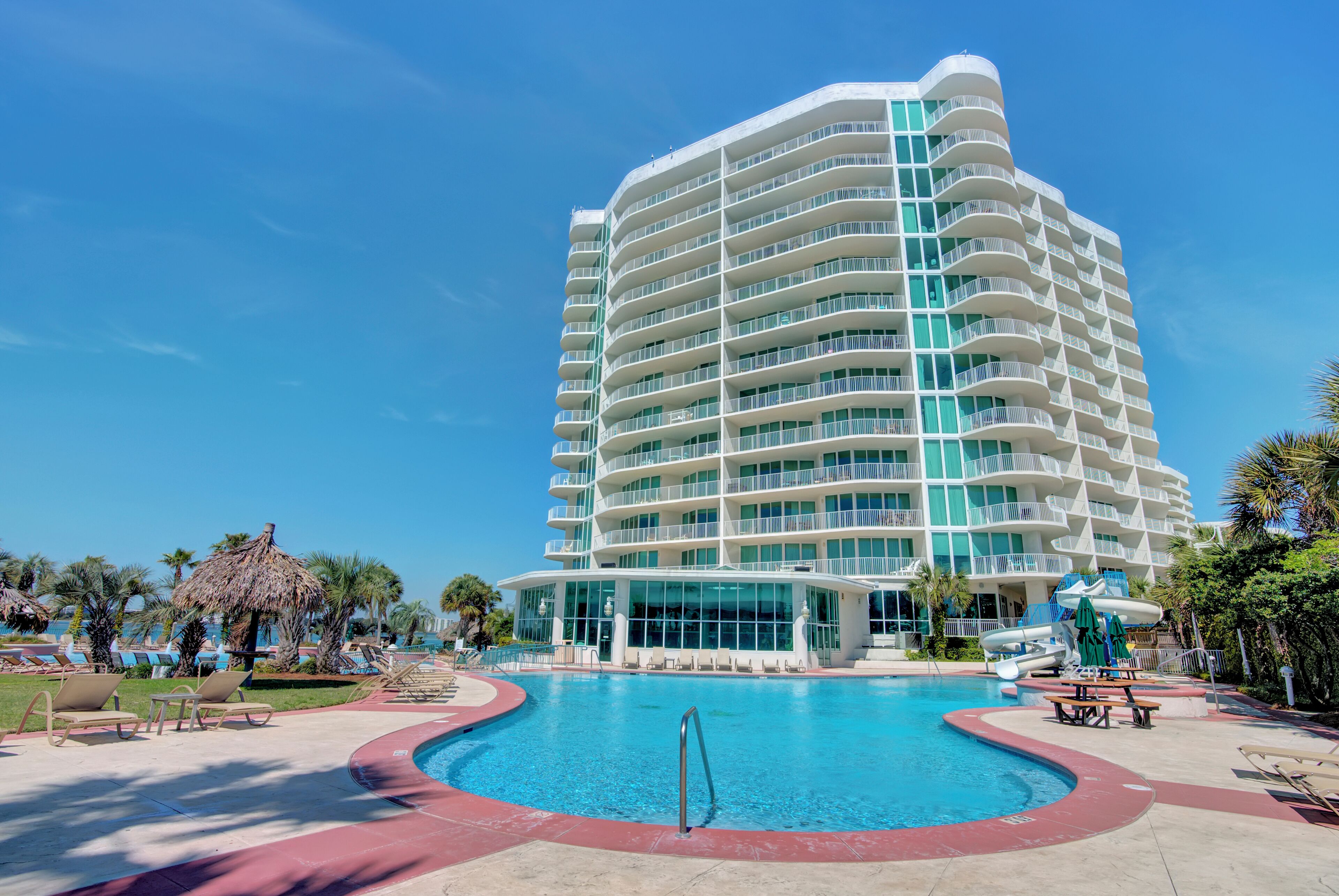 Un hotel grande con piscina, varios balcones y un entorno tropical.
