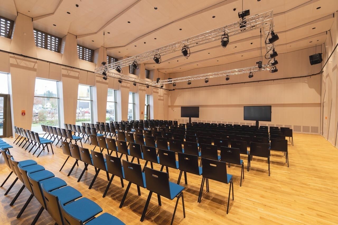 A large conference room with rows of chairs, a stage with lighting equipment, and two large screens.