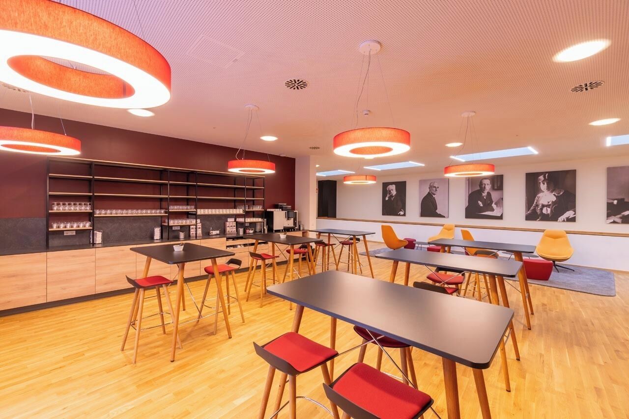 Una cafetería moderna con suelos de madera, sillas rojas y amarillas, y lámparas colgantes redondas.
