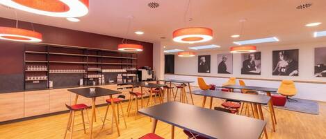 Una cafetería moderna con suelos de madera, sillas rojas y amarillas, y lámparas colgantes redondas.
