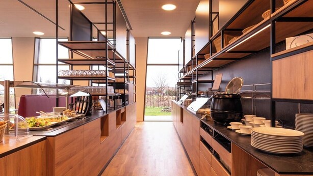 A modern kitchen with wooden cabinets, a long counter, and a view of the outdoors. - BDB-Kulturhotel (Staufen im Breisgau)