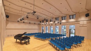 A concert hall with a grand piano, rows of blue chairs, and a stage with lighting equipment. - BDB-Kulturhotel (Staufen im Breisgau)