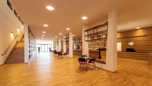 A spacious lobby with wooden flooring, a staircase, and a reception area with a counter and shelves. - BDB-Kulturhotel (Staufen im Breisgau)