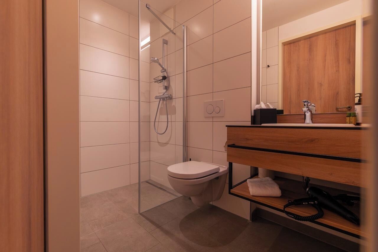 Un baño moderno con cabina de ducha de vidrio, tocador de madera y retrete blanco.