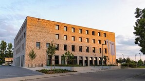 A modern building with a brick facade, multiple windows, and a paved entrance area with a small tree. - BDB-Kulturhotel (Staufen im Breisgau)
