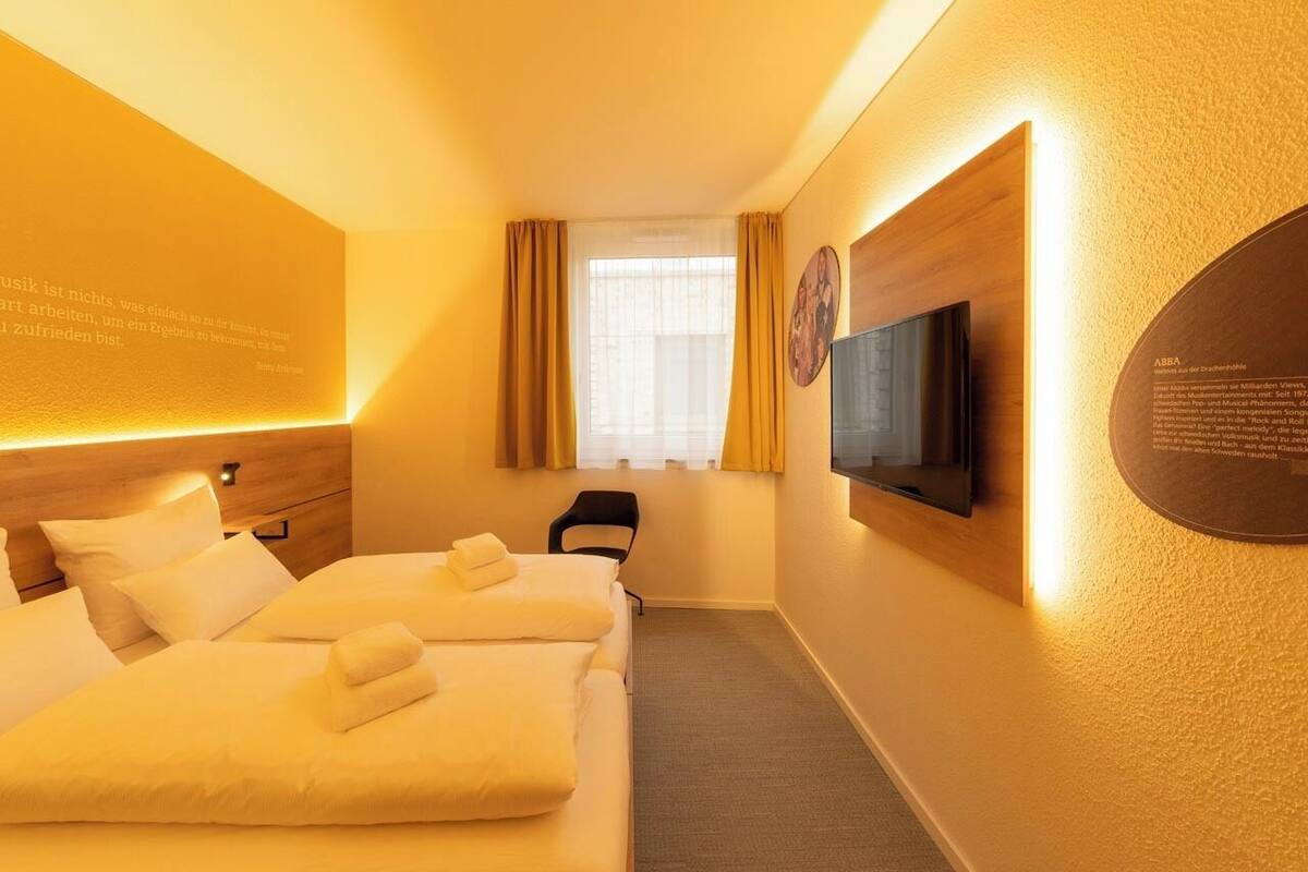 Une chambre d’hôtel avec deux lits, un téléviseur à écran plat fixé au mur et une fenêtre avec des rideaux.