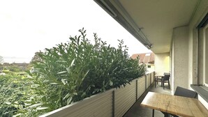 Un balcón con una mesa y sillas de madera, baranda metálica y vistas a zonas verdes y edificios.