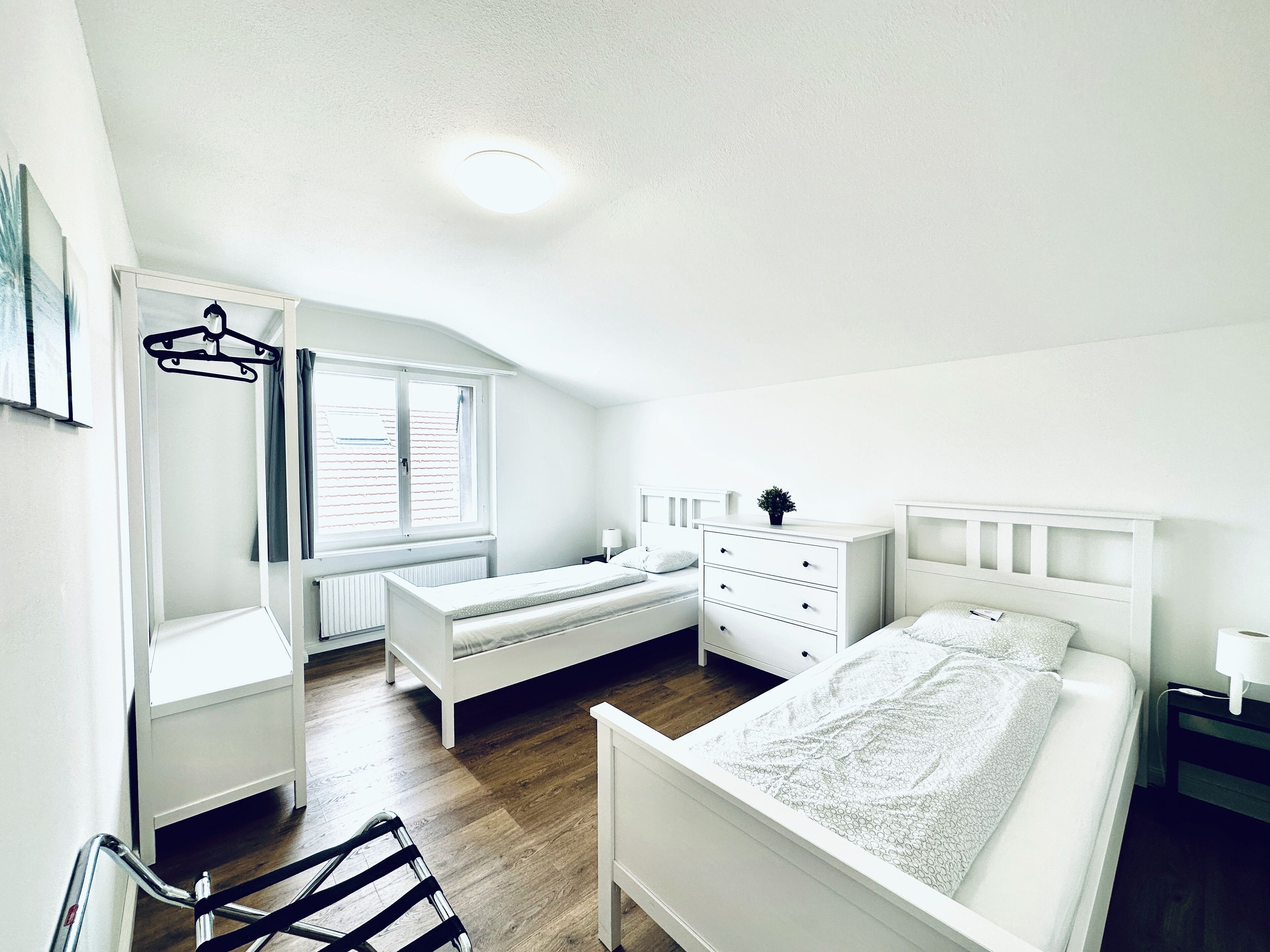 Un dormitorio con cama, cómoda, mesita de noche, radiador y ventana con cortinas.