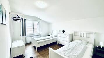Un dormitorio con cama, cómoda, mesita de noche, radiador y ventana con cortinas.