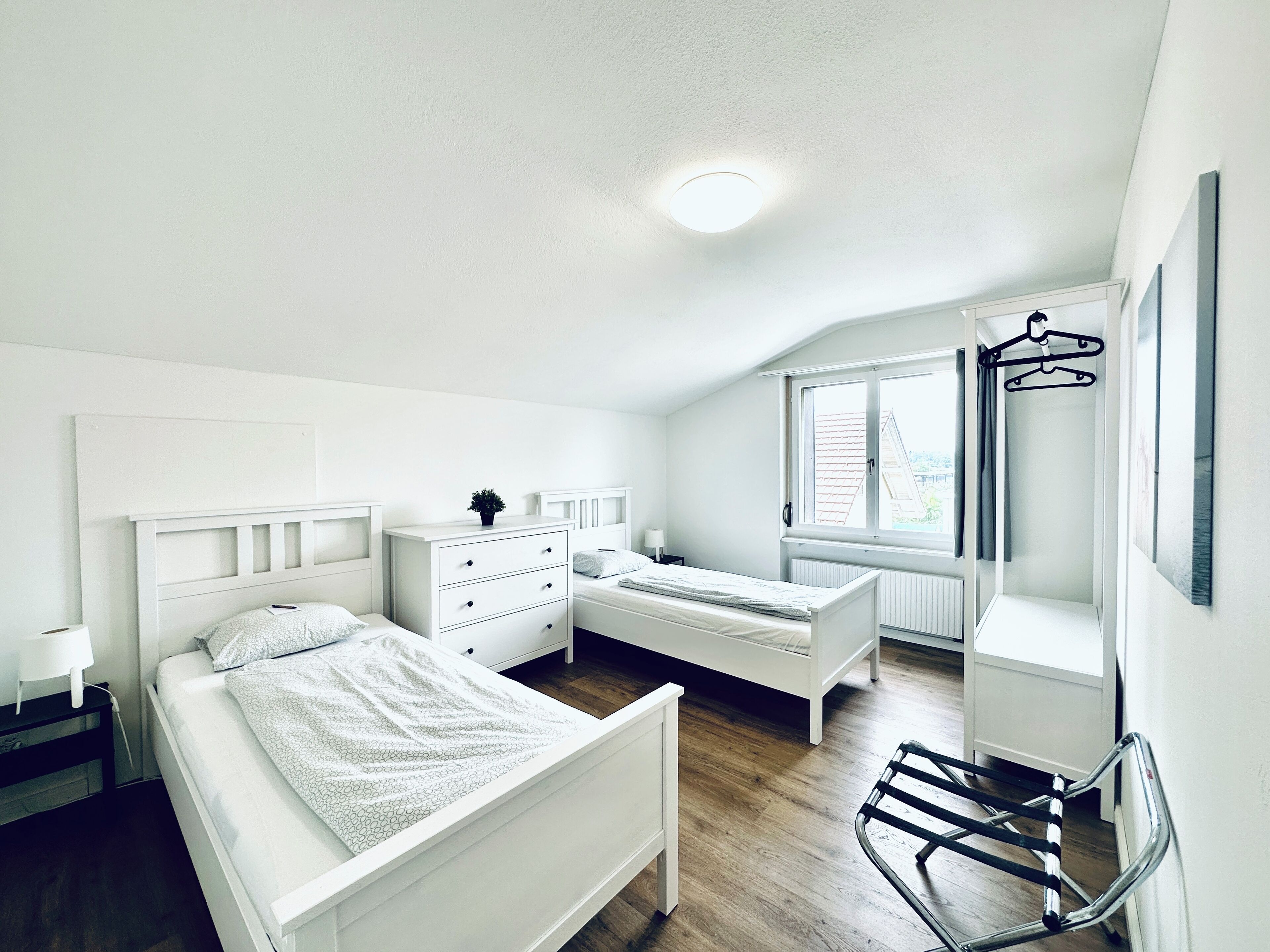 A bedroom with a bed, a dresser, a chair, a window, and a radiator.