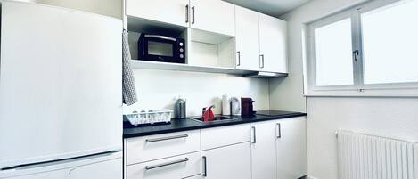 A modern kitchen with white cabinets, a black microwave, and a window providing natural light.