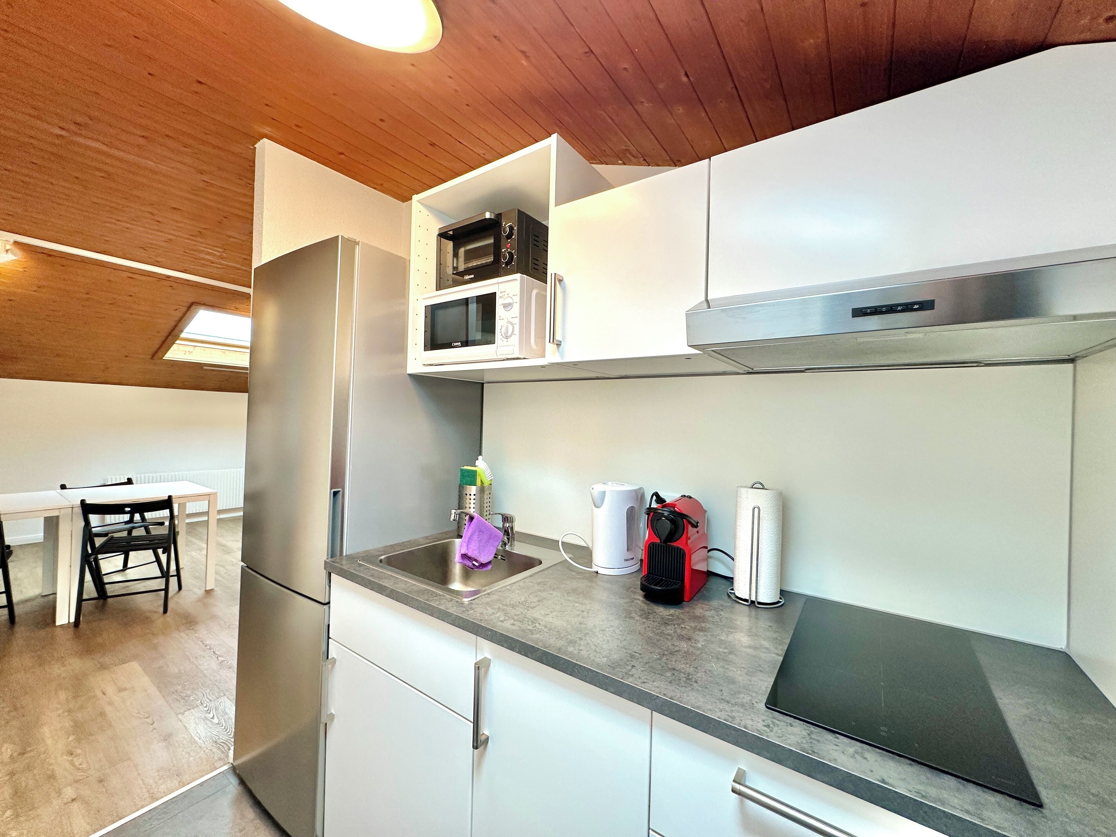 A modern kitchen with white cabinets, a built-in microwave, a stainless steel range hood, and a black induction cooktop.