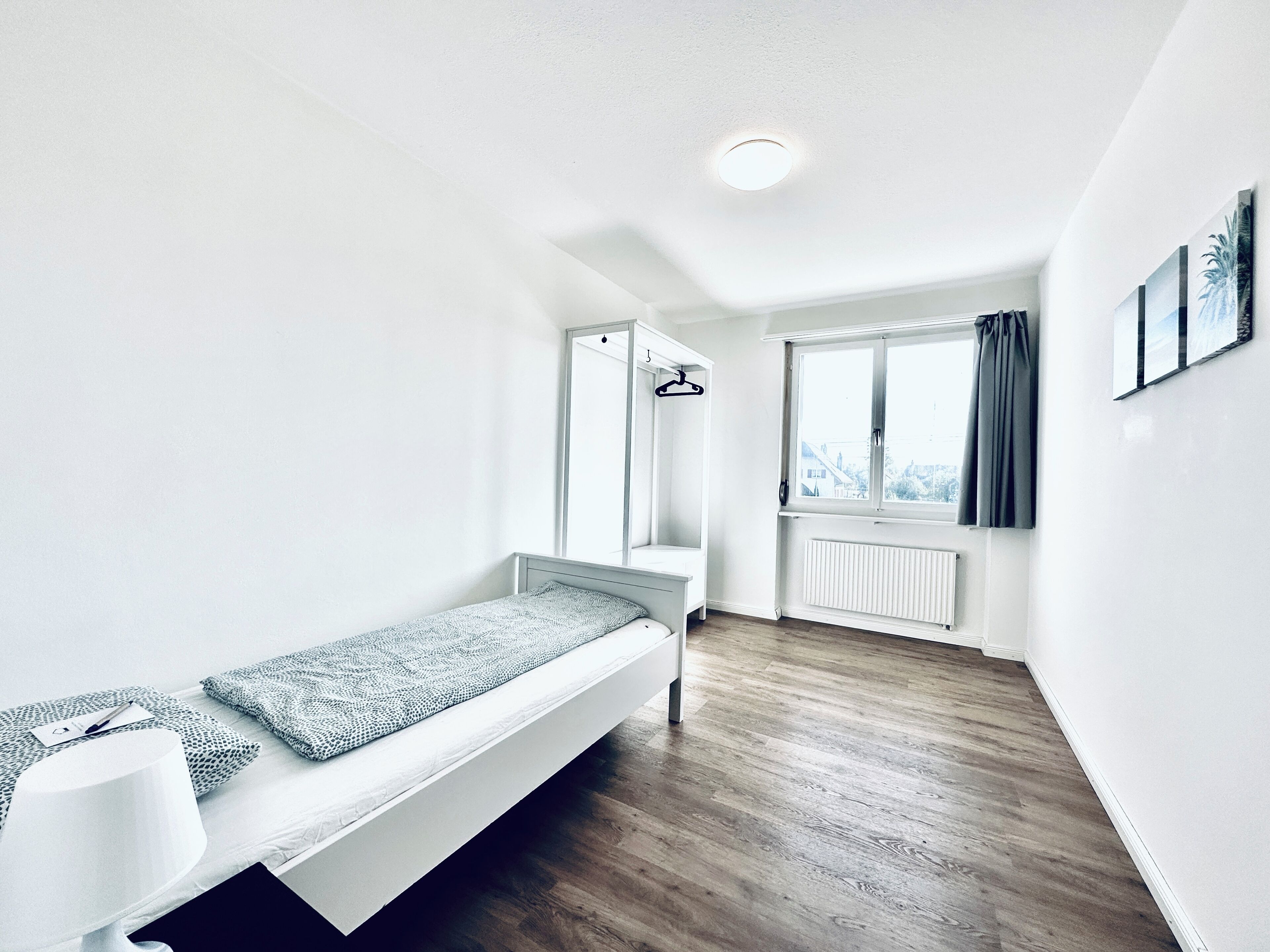 A minimalist bedroom with a single bed, a bedside table, and a window with curtains.
