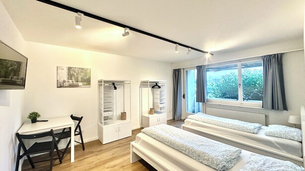Un dormitorio moderno con escritorio, dos camas, un armario y una ventana con cortinas.
