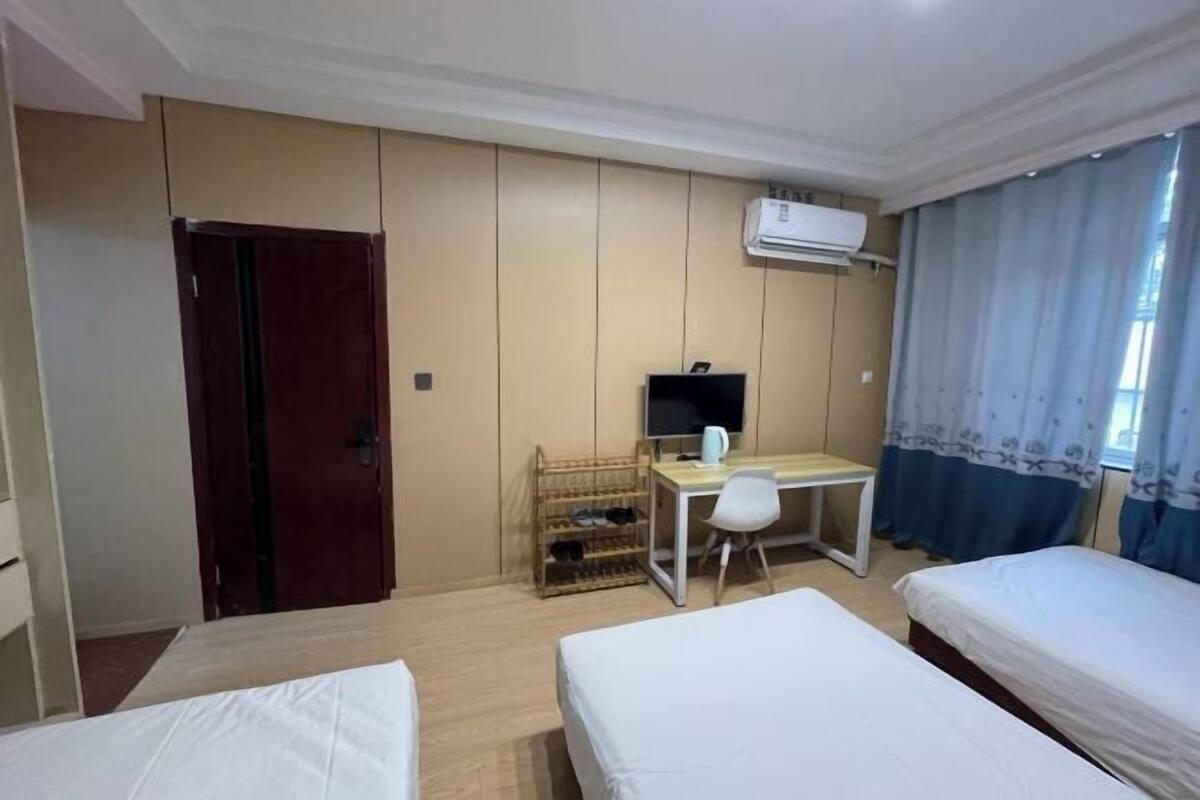 A hotel room with two beds, a desk with a chair, a TV, and an air conditioning unit.