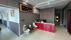Een hotel receptie met een rode balie, een kunstwerk erboven en een zithoek met twee stoelen.
