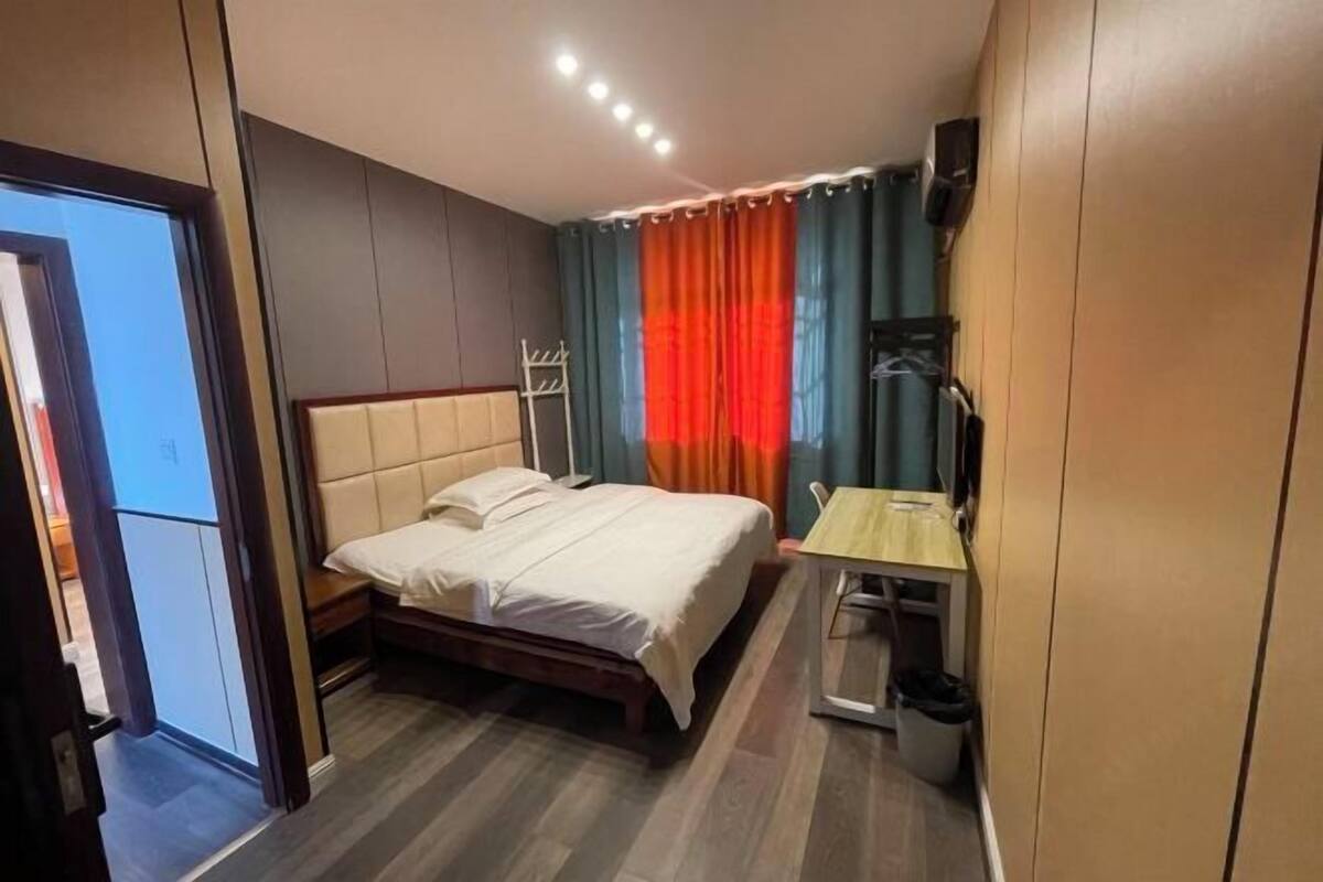 A hotel room with a bed, a desk, a chair, a TV, and a window with curtains.