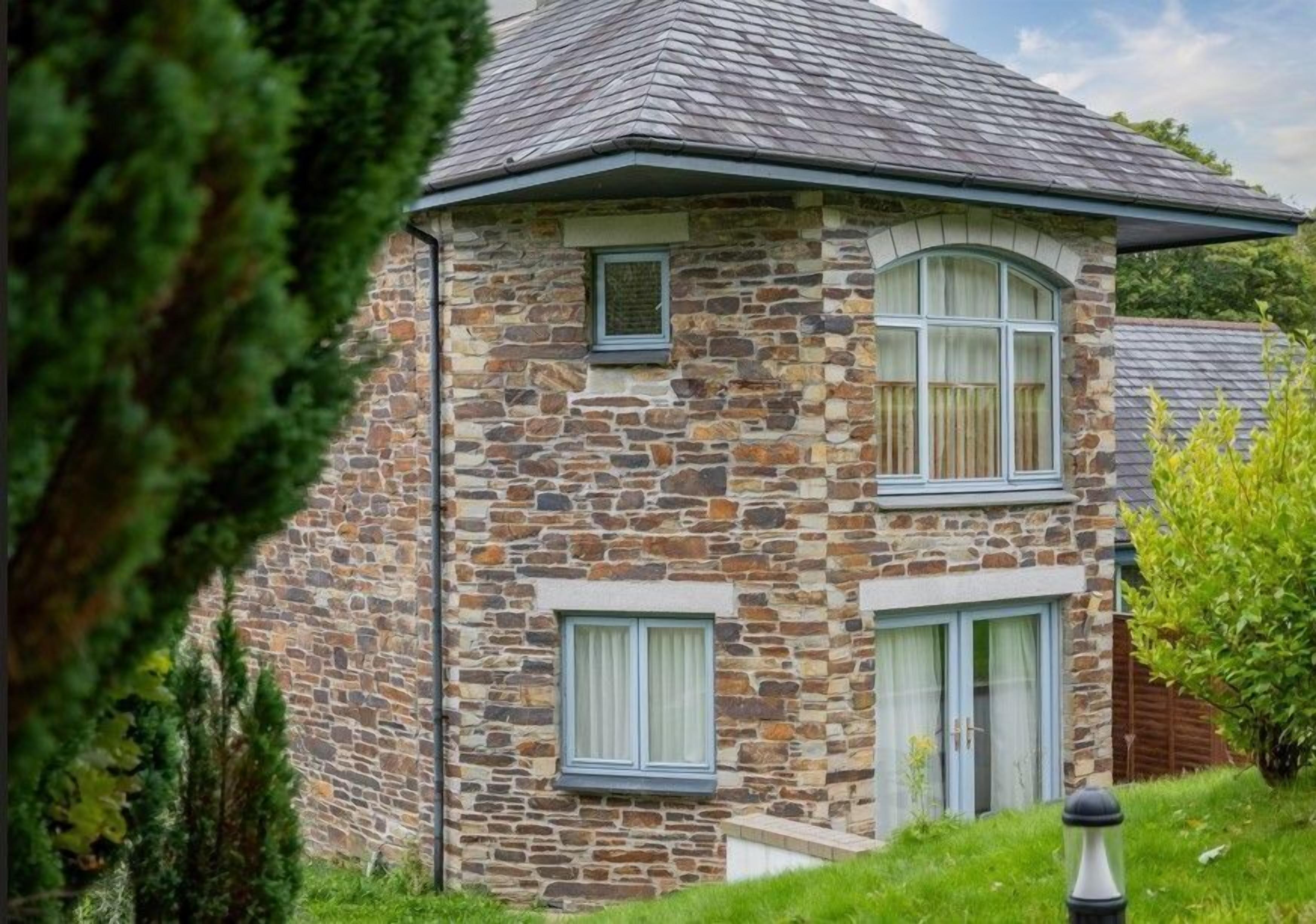 A stone house with a gabled roof, two windows with shutters, and a small porch area.