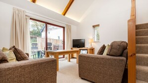 A modern living room with two brown sofas, a wooden table, a TV, and a staircase.
