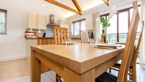 A modern kitchen with wooden beams, a dining table set for four, and a large window with a view.
