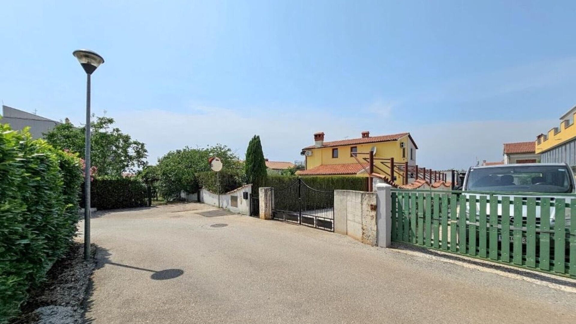 Une allée bordée de portails mène à une maison jaune avec un toit rouge, entourée de verdure et d’un lampadaire.