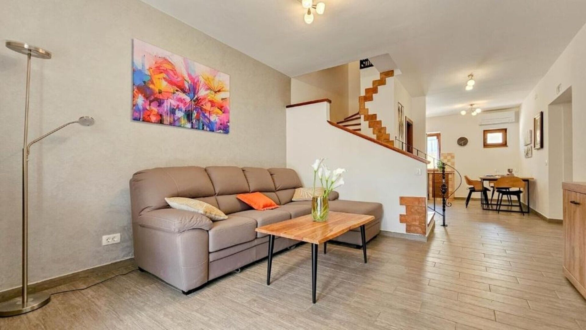 A living room with a brown sofa, a wooden coffee table, and a colorful abstract painting on the wall.