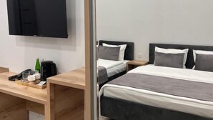 A modern bedroom with a bed, a wooden desk, a flat-screen TV, and a mirror.