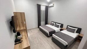 A hotel room with two beds, a wooden dresser, a TV, and an air conditioning unit.