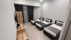 A modern hotel room with three beds, a wooden desk, and a large window with curtains.