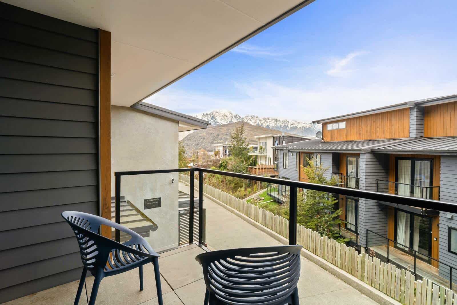 A balcony with two chairs, a view of neighboring houses, and a wooden fence.