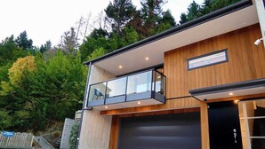 A modern two-story building with a wooden facade, a balcony with glass railings, and a garage door. - Grand Alpine Villa - 4 bedrooms (Queenstown)