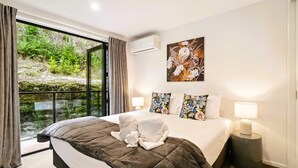 A hotel room with a large bed, a view of greenery through a sliding door, a painting on the wall, and a bedside lamp. - Grand Alpine Villa - 4 bedrooms (Queenstown)